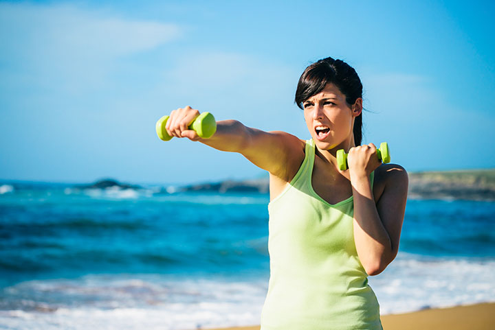 woman on beach exercising with dumbbells 